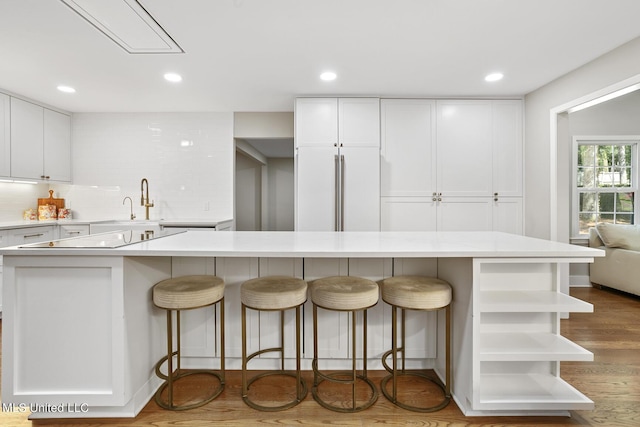 kitchen featuring open shelves, decorative backsplash, white cabinetry, wood finished floors, and a kitchen breakfast bar