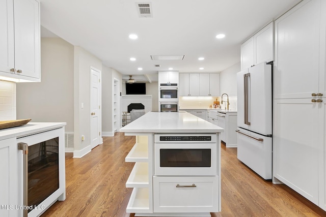 kitchen featuring wine cooler, double wall oven, a fireplace, visible vents, and freestanding refrigerator