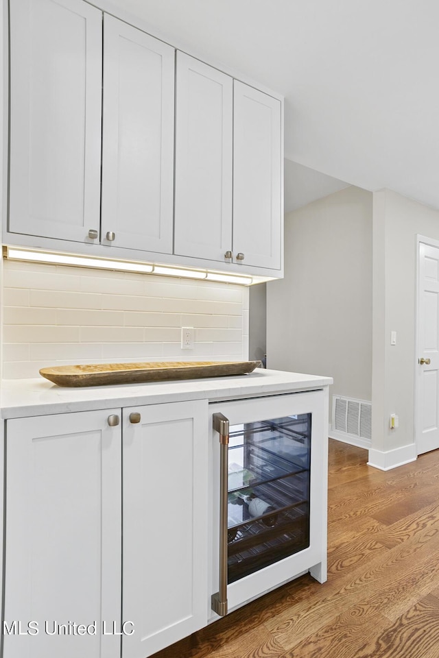 bar with beverage cooler, baseboards, visible vents, light wood-style flooring, and backsplash