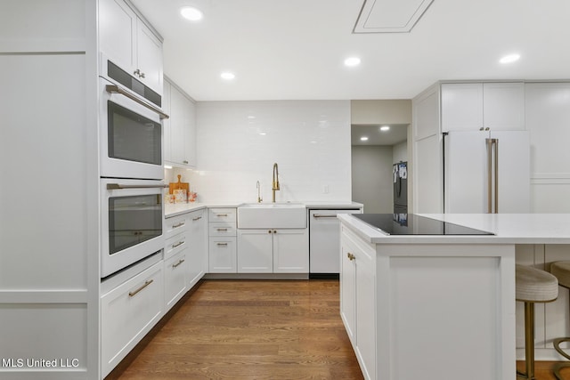 kitchen with dark wood-style floors, decorative backsplash, a sink, white appliances, and a kitchen breakfast bar