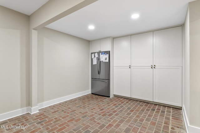 interior space with white cabinetry, brick floor, freestanding refrigerator, and baseboards