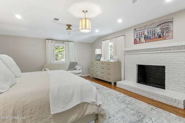 bedroom with a brick fireplace, visible vents, multiple windows, and wood finished floors