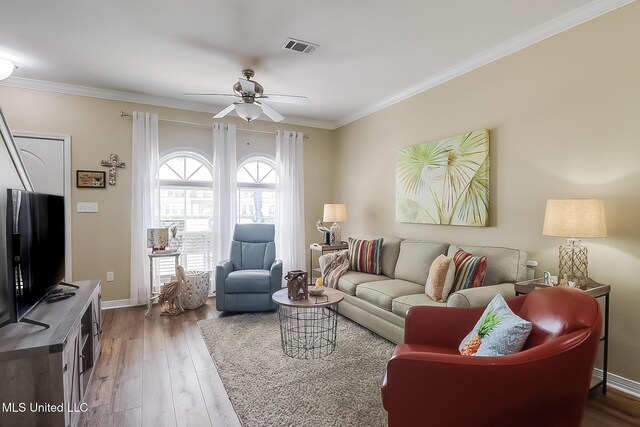 living area with visible vents, baseboards, wood finished floors, ceiling fan, and ornamental molding
