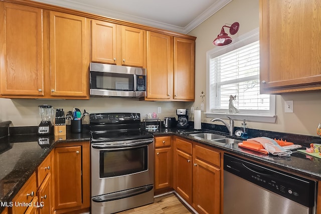 kitchen with stainless steel appliances, a sink, dark stone countertops, brown cabinets, and crown molding