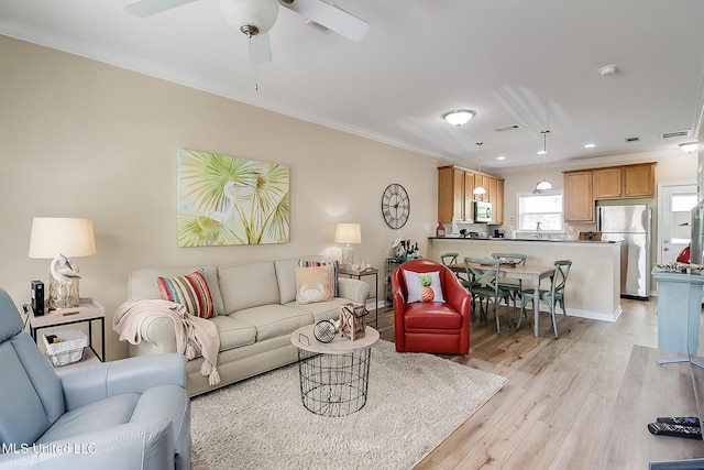 living room with light wood-type flooring, visible vents, crown molding, and ceiling fan