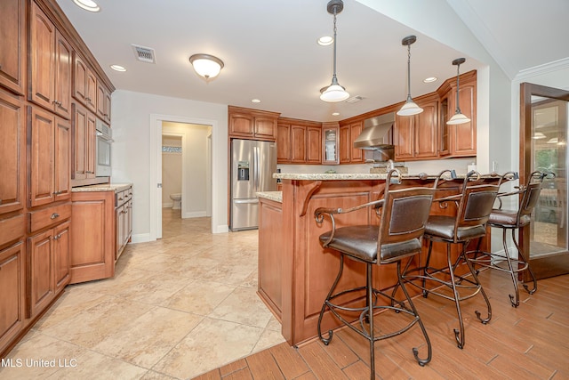 kitchen with stainless steel refrigerator with ice dispenser, a peninsula, a breakfast bar, brown cabinetry, and wall chimney exhaust hood