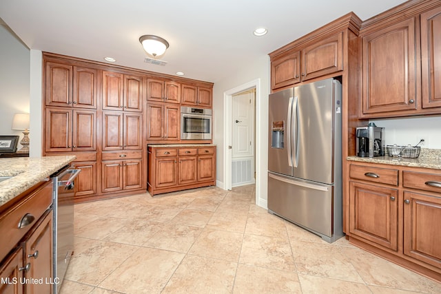 kitchen with stainless steel appliances, brown cabinetry, light stone counters, and recessed lighting