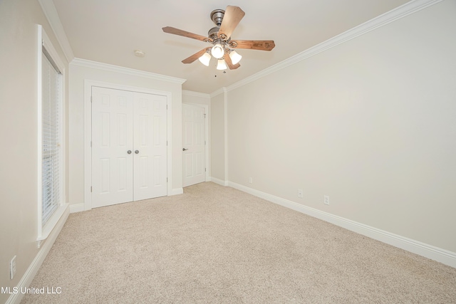 unfurnished bedroom featuring crown molding, carpet, a closet, baseboards, and ceiling fan
