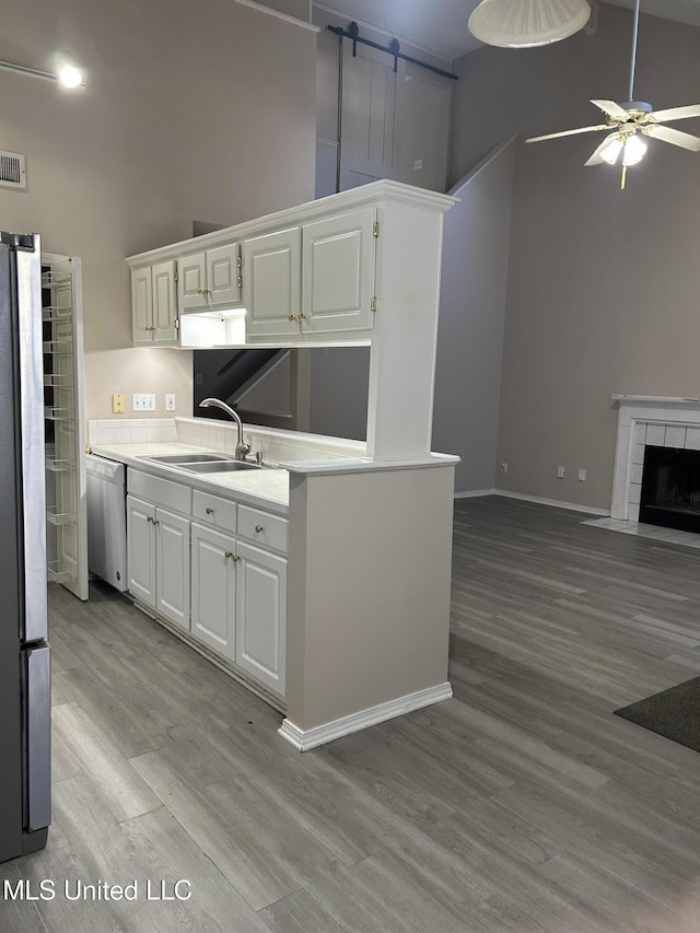 kitchen featuring high vaulted ceiling, white cabinets, sink, light wood-type flooring, and stainless steel appliances