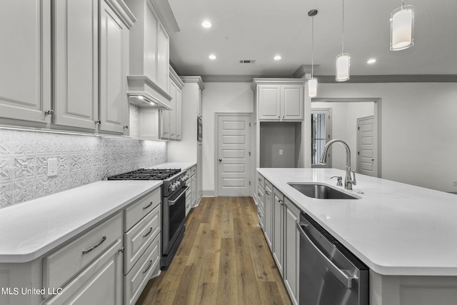 kitchen with appliances with stainless steel finishes, sink, an island with sink, decorative light fixtures, and dark hardwood / wood-style floors