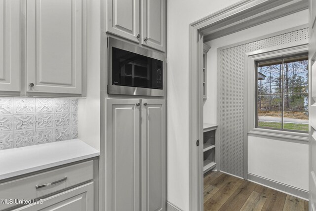 kitchen featuring stainless steel microwave, dark wood-type flooring, and backsplash