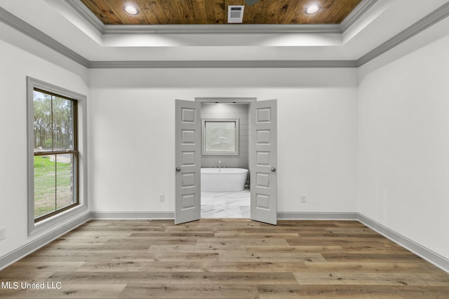 unfurnished bedroom with ensuite bath, a raised ceiling, ornamental molding, and light hardwood / wood-style floors