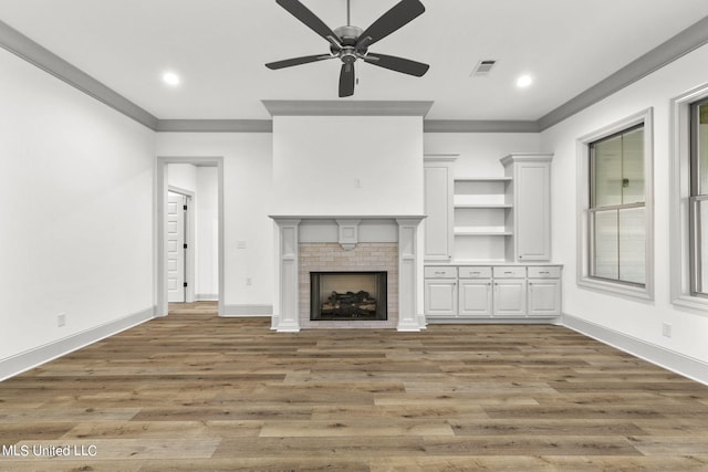 unfurnished living room featuring crown molding, a brick fireplace, dark hardwood / wood-style floors, and ceiling fan