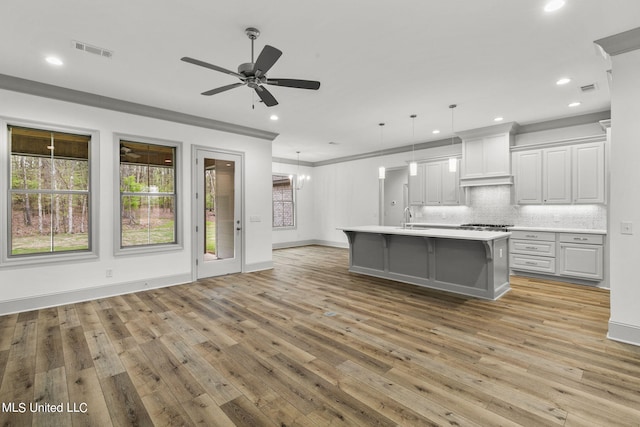 kitchen featuring sink, light wood-type flooring, pendant lighting, ornamental molding, and a center island with sink