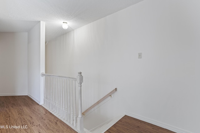 stairway featuring a textured ceiling, baseboards, and wood finished floors