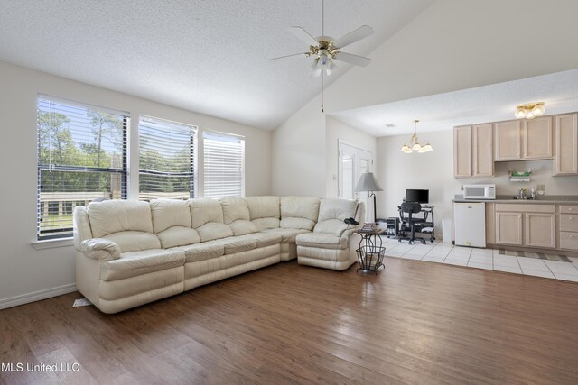 living room with light wood-style floors, baseboards, ceiling fan with notable chandelier, and high vaulted ceiling