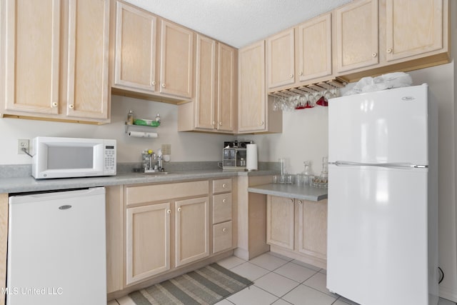 kitchen featuring white appliances, light tile patterned floors, light brown cabinetry, and a sink