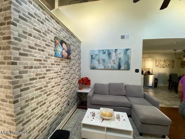 living room with visible vents, brick wall, a high ceiling, and a ceiling fan