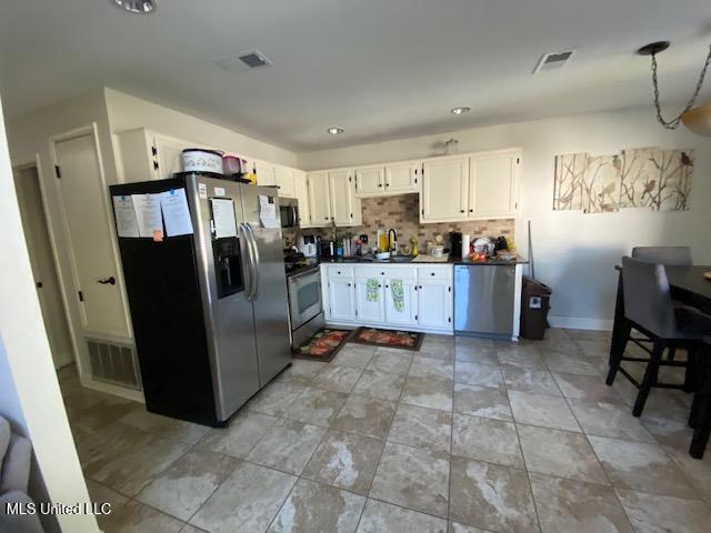 kitchen featuring visible vents, stainless steel appliances, decorative backsplash, white cabinets, and dark countertops