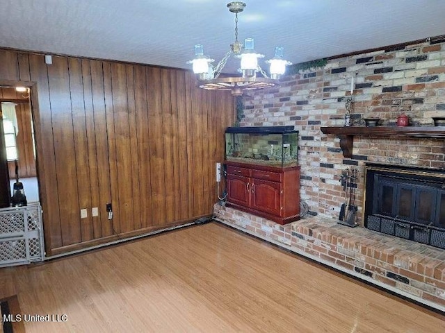 living room featuring a chandelier, a brick fireplace, light hardwood / wood-style floors, and wood walls