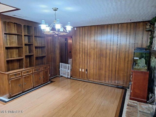 unfurnished dining area featuring an inviting chandelier, wooden walls, a textured ceiling, and light wood-type flooring