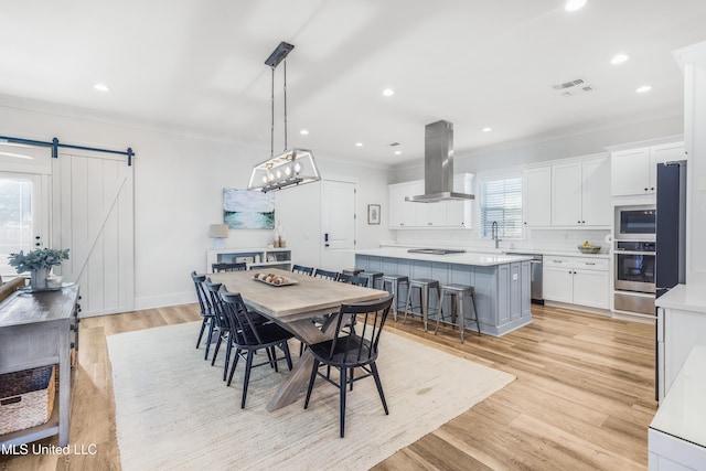 dining space with a barn door, light hardwood / wood-style floors, and ornamental molding