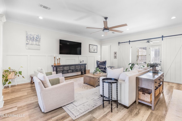 living room featuring a barn door, light wood-type flooring, and ornamental molding