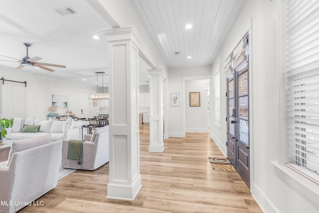 entryway with ornate columns, ceiling fan, a barn door, and light wood-type flooring