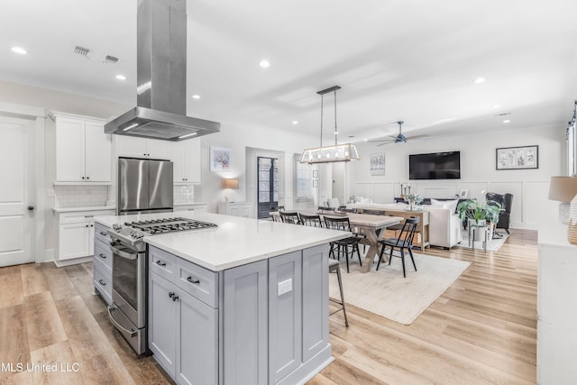 kitchen with ceiling fan, hanging light fixtures, island range hood, a kitchen island, and appliances with stainless steel finishes