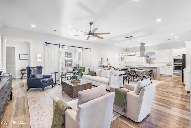 living room featuring ceiling fan, a barn door, light hardwood / wood-style floors, and ornamental molding