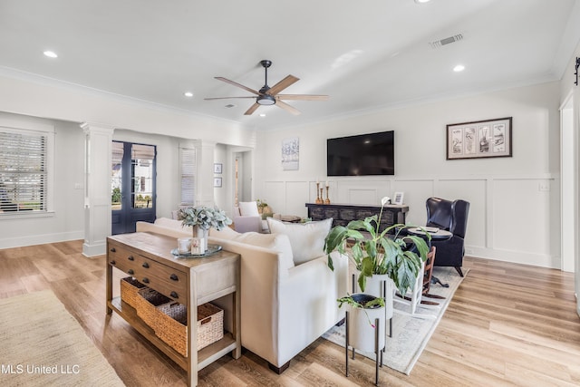 living room with ceiling fan, light wood-type flooring, crown molding, and decorative columns