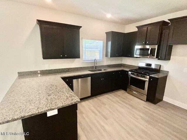 kitchen featuring kitchen peninsula, sink, light hardwood / wood-style flooring, light stone countertops, and appliances with stainless steel finishes