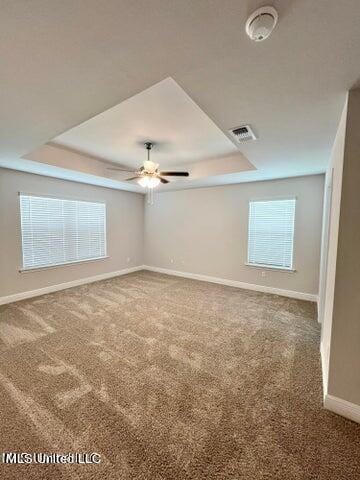 empty room with carpet, ceiling fan, and a tray ceiling