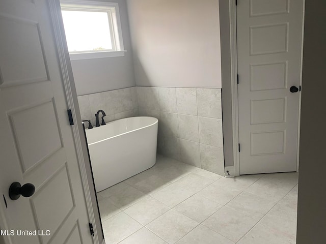 bathroom with tile patterned flooring, a washtub, and tile walls