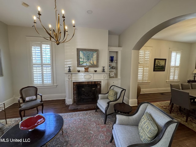 living area with a fireplace, wood finished floors, arched walkways, and baseboards