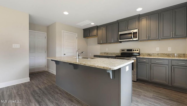 kitchen with recessed lighting, stainless steel appliances, a sink, dark wood-style floors, and a center island with sink