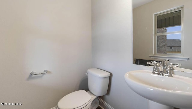 half bath featuring toilet, baseboards, and a sink