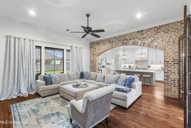 living room with crown molding, wood-type flooring, ceiling fan, and brick wall