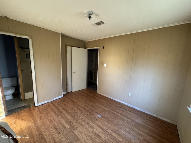 unfurnished bedroom featuring hardwood / wood-style flooring, wood walls, and ensuite bath