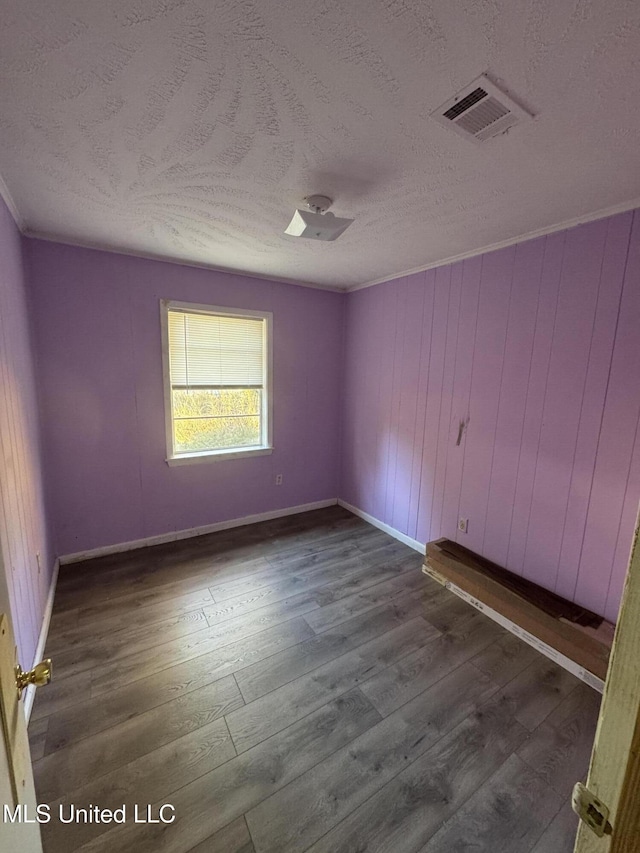 empty room featuring wood walls, dark hardwood / wood-style flooring, and a textured ceiling