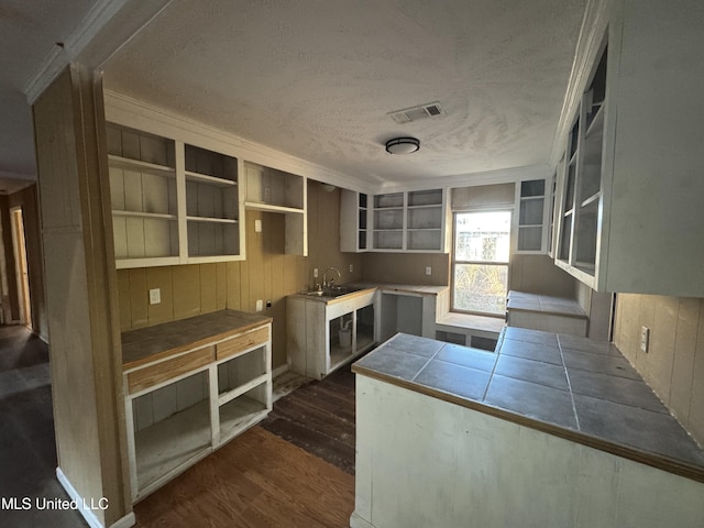 kitchen featuring a textured ceiling, tile counters, crown molding, and dark wood-type flooring