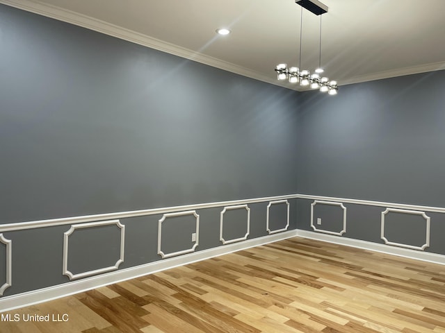 empty room featuring hardwood / wood-style flooring, ornamental molding, and a chandelier