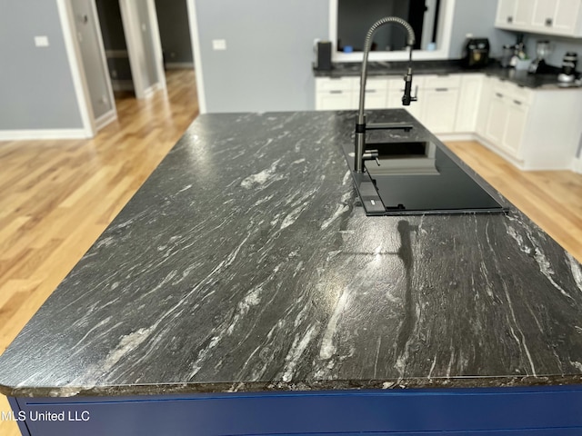 kitchen with wood-type flooring, sink, white cabinets, and dark stone counters