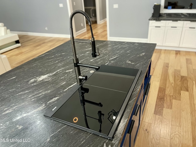 interior details featuring white cabinetry, sink, dark stone countertops, and light hardwood / wood-style floors