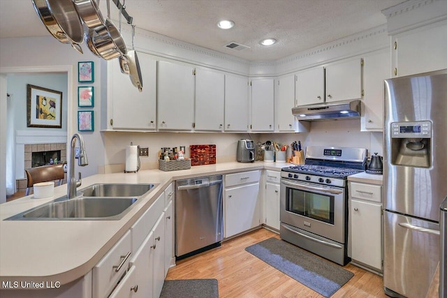 kitchen featuring light wood finished floors, under cabinet range hood, light countertops, appliances with stainless steel finishes, and a sink