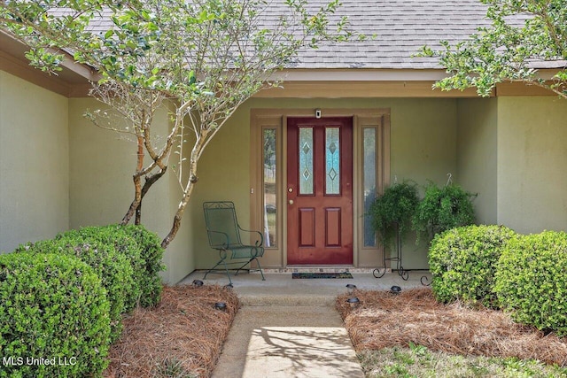 entrance to property with stucco siding and a shingled roof