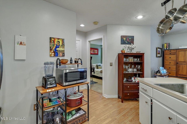 kitchen featuring stainless steel microwave, recessed lighting, light wood-style floors, white cabinets, and light countertops