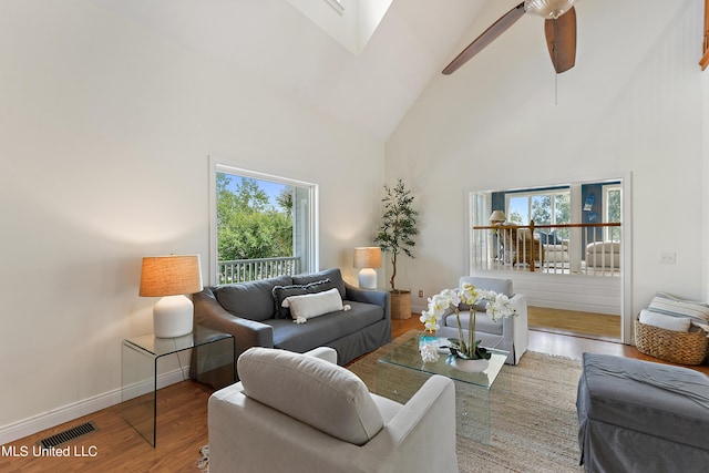 living room featuring hardwood / wood-style flooring, ceiling fan, a skylight, and high vaulted ceiling