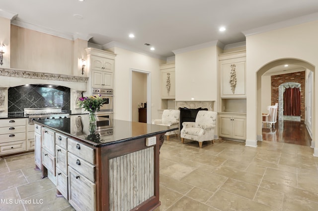 kitchen featuring a kitchen island, cream cabinets, crown molding, appliances with stainless steel finishes, and tasteful backsplash