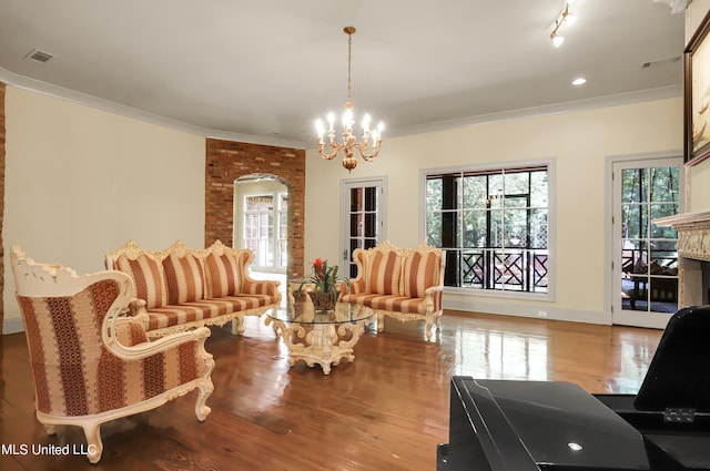 living room with a large fireplace, a notable chandelier, ornamental molding, and light hardwood / wood-style flooring